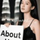 Woman in black dress holding an "About Us" sign with city lights in the background